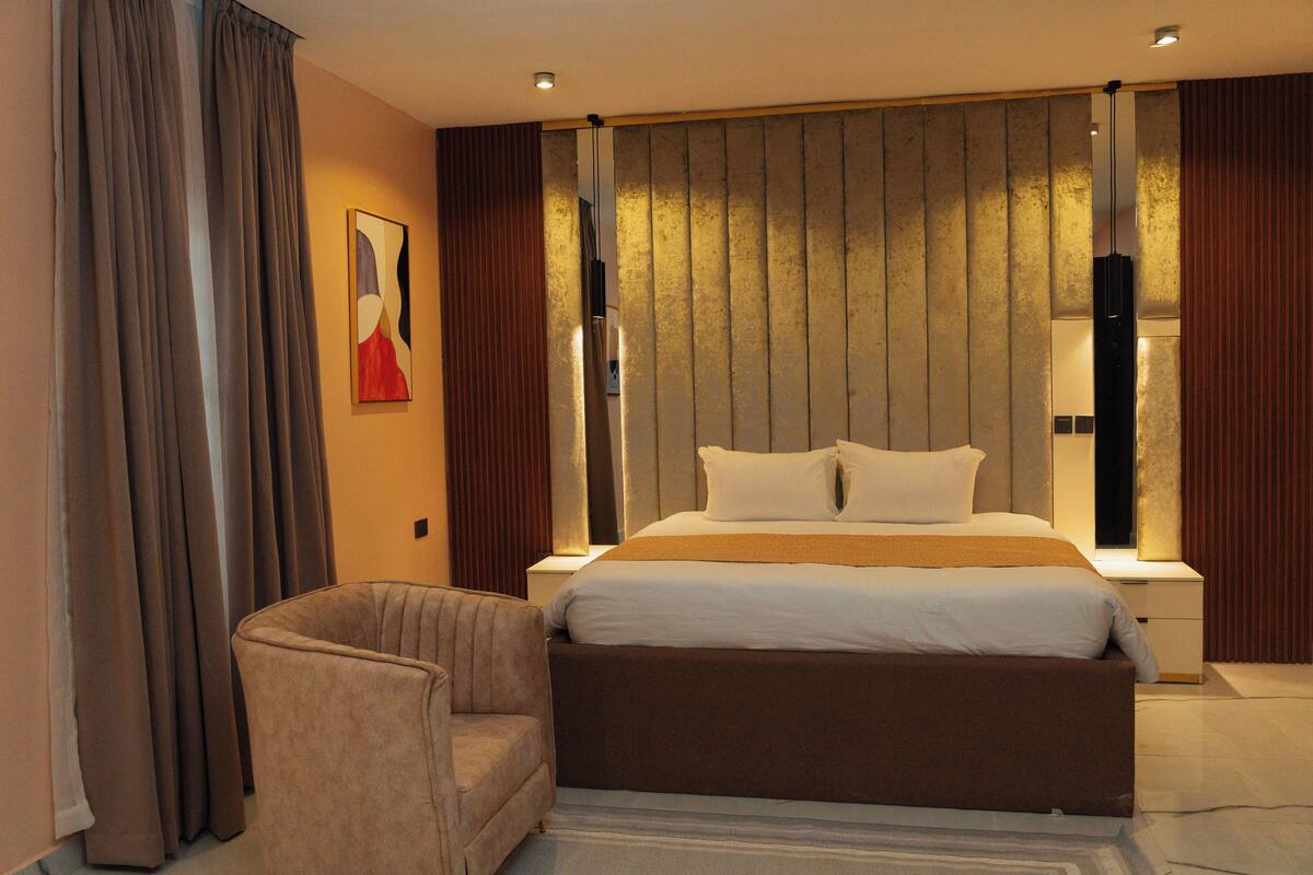 A modern hotel room with a large bed, a chair, and a painting on the wall.