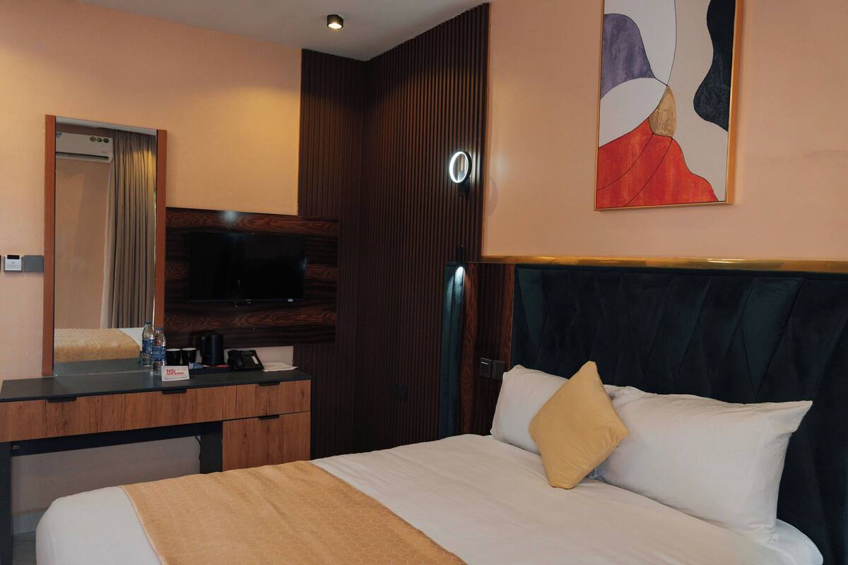 A hotel room with a bed, a desk, a TV, a mirror, and a wall art piece.