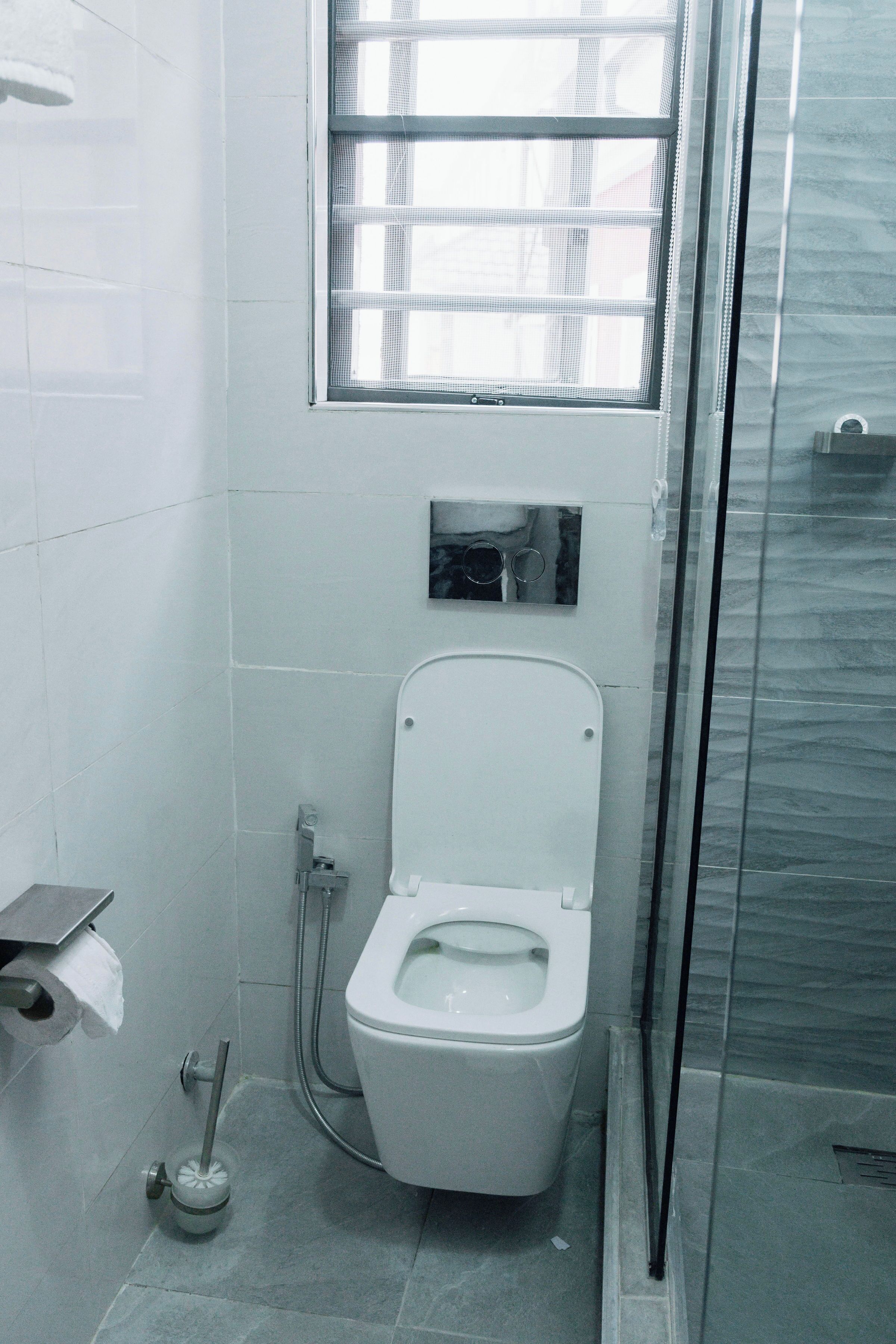 A bathroom with a toilet, a hand dryer, and a window.
