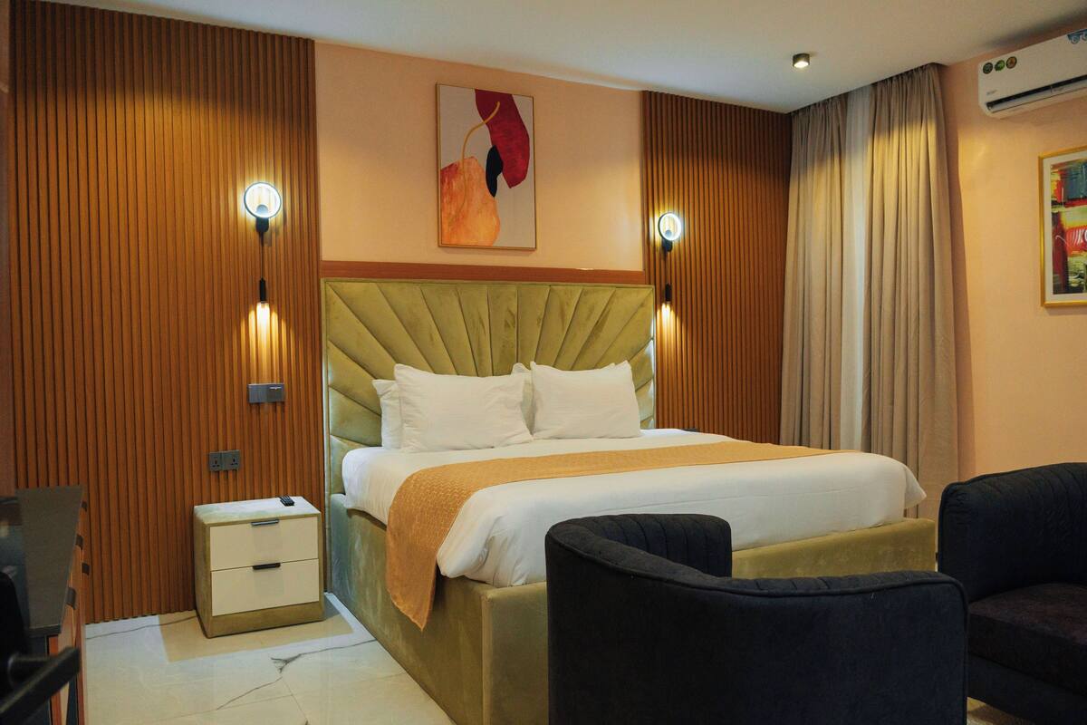 A hotel room with a bed, bedside tables, a chair, and a wall-mounted light fixture.