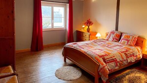 A bedroom with a wooden bed, a nightstand with a lamp, a window with red curtains, and a wooden floor. - Cozy cottage with sauna, near Loire castles (Pouillé)