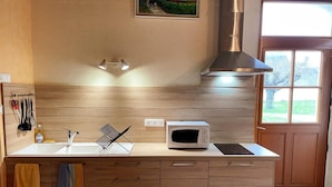 A kitchen with wooden cabinets, a white countertop, a microwave, a sink, and a stainless steel range hood. - Cozy cottage with sauna, near Loire castles (Pouillé)