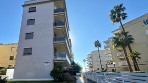 A multi-story building with balconies, a gated entrance, and palm trees.