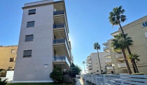 Un edificio de varios pisos con balcones, una entrada con reja y palmeras.