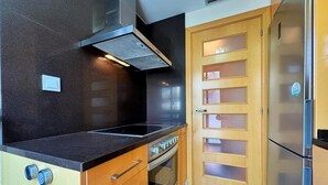 A kitchen with a black countertop, a stainless steel range hood, a wooden door with frosted glass panels, and a refrigerator.