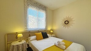 A hotel room with a bed, two bedside tables with lamps, a decorative wall piece, and a window with patterned curtains.