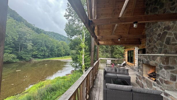 Une terrasse en bois, meublée de mobilier en osier, qui offre une vue sur une rivière et des collines boisées.