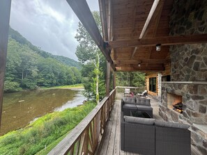 Une terrasse en bois, meublée de mobilier en osier, qui offre une vue sur une rivière et des collines boisées.