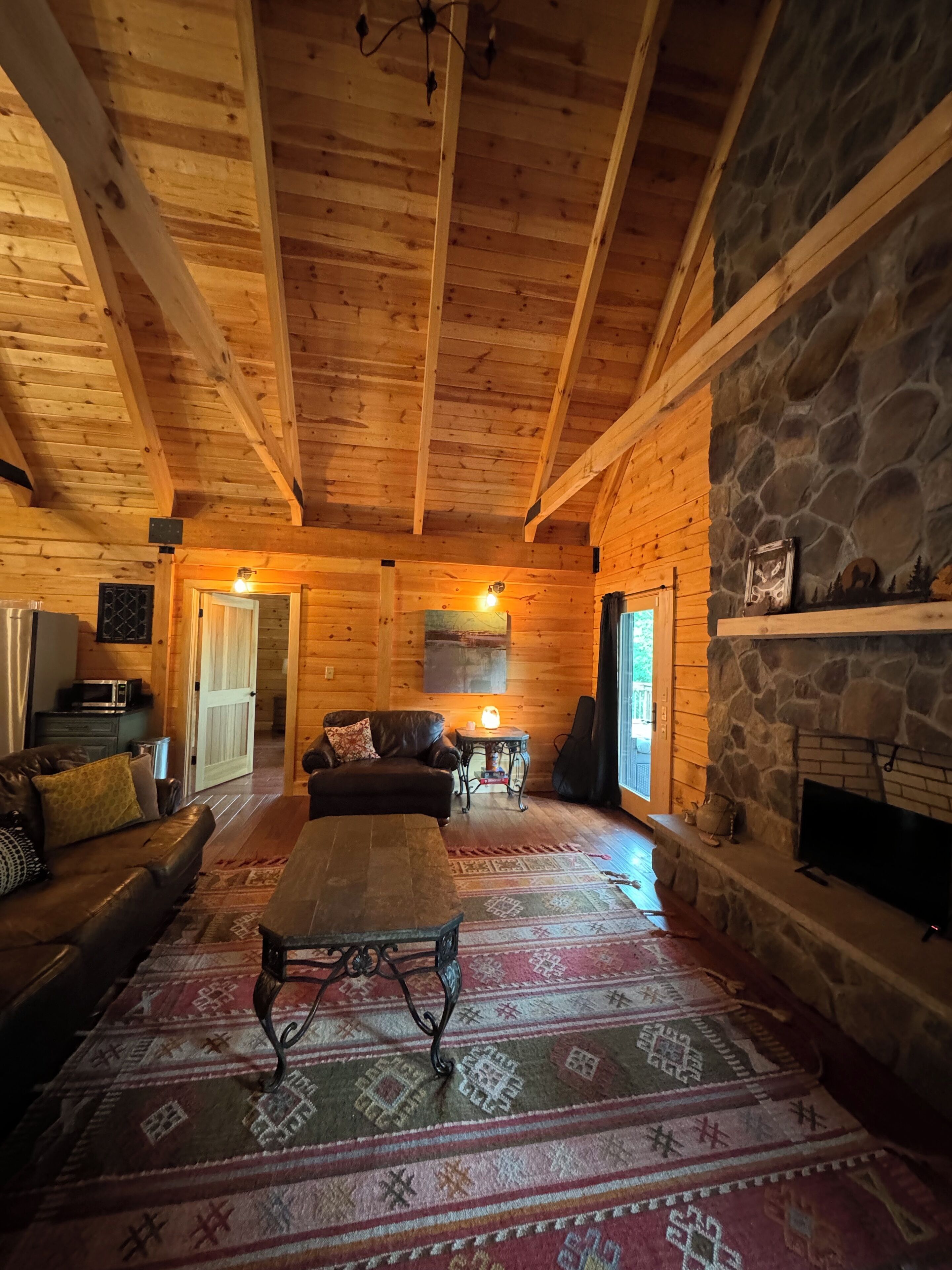 L’intérieur d’un chalet confortable, avec une cheminée en pierre, des poutres en bois au plafond, un canapé en cuir et un tapis à motifs.