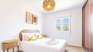 Ein Schlafzimmer mit einem Bett, Nachttischen, einer Pendelleuchte, einem Fenster mit Blick und gerahmten Kunstwerken an der Wand.