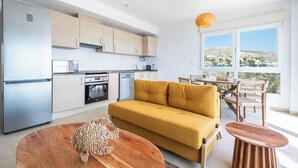 Eine moderne Küche mit Edelstahlgeräten, einem senffarbenen Sofa und einem Essbereich mit Korbstühlen.