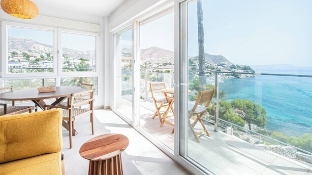 Ein modernes Wohnzimmer mit Essbereich, großen Fenstern und einem Balkon mit Meerblick.