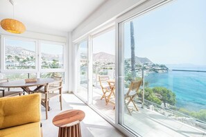 A modern living room with a dining area, large windows, and a balcony with a view of the sea. - Ópalo Oceanfront Apartment & Terrace (El Campello)