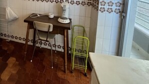 Una cucina con schienale piastrellato, un tavolo con sedie, una mensola metallica verde e un piano di lavoro bianco.