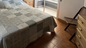 Una camera da letto con un letto coperto da una coperta a quadri, un comò in legno e una sedia.