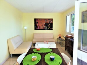 Een eetgedeelte met een tafel, stoelen, een bank, een schilderij aan de muur en een raam.