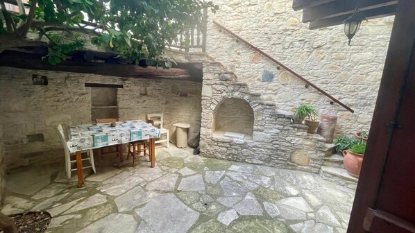 Une cour pavée de pierres, avec une table et des chaises, une petite arche et des plantes en pot.