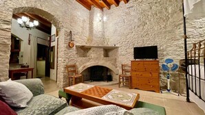 A stone-walled living room with a fireplace, a television, and a chessboard on a table. - Juliet Studio Suite by TrulyCyprus (Dhoros)
