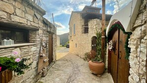 A narrow stone pathway leading to a rustic building with a wooden door decorated with greenery. - Juliet Studio Suite by TrulyCyprus (Dhoros)
