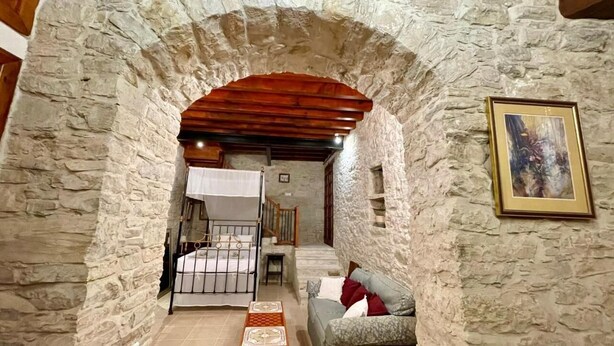 A stone-walled room with a wooden ceiling, a bed, a sofa, and a framed picture on the wall. - Juliet Studio Suite by TrulyCyprus (Dhoros)