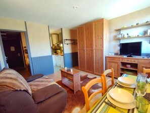 A compact living space with a sofa, dining table, chairs, a kitchen area, and a television.