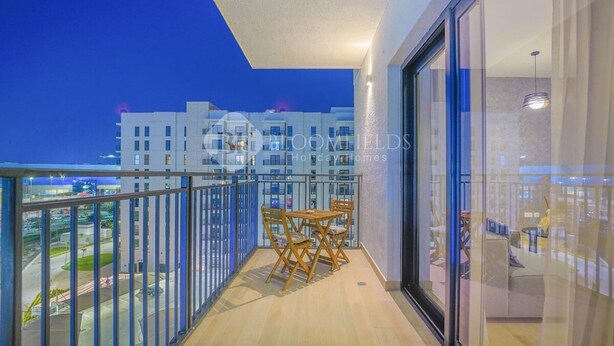 Ein Balkon mit Tisch und Stühlen, eine Glastür und Blick auf Gebäude im Hintergrund.