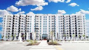 Ein modernes, mehrstöckiges Hotel mit zentralem Eingang, umgeben von begrünten Flächen und blauem Himmel.