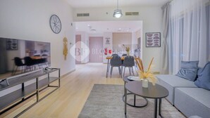 Ein modernes Wohnzimmer mit einer Couch, einem Couchtisch und einem Fernseher. Im Hintergrund ist ein Essbereich mit Stühlen und einem Tisch zu sehen.