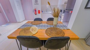 Ein Essbereich mit einem Holztisch, gewebten Platzsets, zwei schwarzen Stühlen und einer Vase mit Trockenpflanzen.