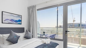 A modern hotel room with a large bed, a balcony with a table and chairs, and a view of the construction site. - Bloomfields New STU in Oasis Masdar City (Abu Dabi)