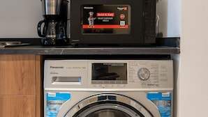 A compact washer and dryer unit with a digital control panel, a coffee maker, and a kettle on top. - Bloomfields New STU in Oasis Masdar City (Abu Dabi)