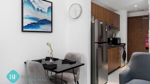 A modern kitchen with stainless steel appliances, a dining area with a table and chairs, and a wall-mounted clock. - Bloomfields New STU in Oasis Masdar City (Abu Dabi)