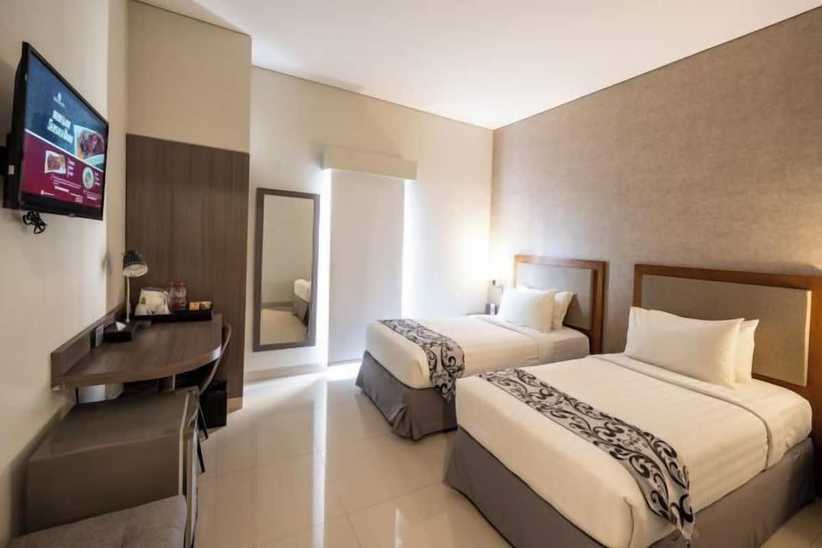 A hotel room with two beds, a desk, a TV, and a mirror.