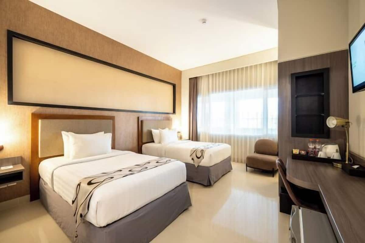 A hotel room with two beds, a desk, a chair, and a TV.