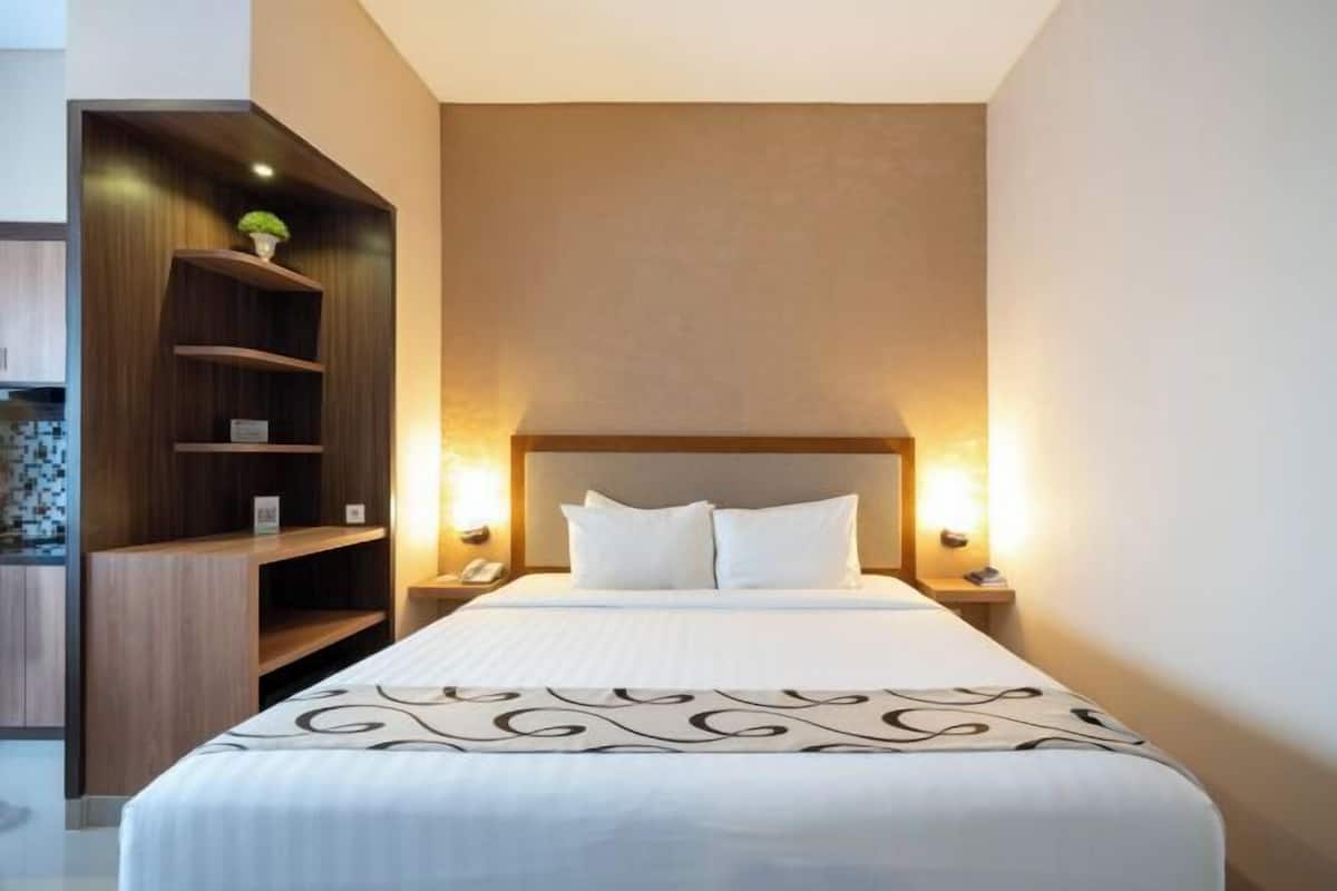 A hotel room with a large bed, two bedside tables, a wooden shelving unit, and wall-mounted lights.