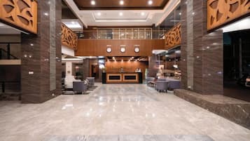 Een hotel lobby met een receptiebalie, een zithoek en een trap.