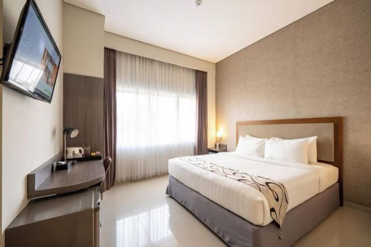 A hotel room with a bed, bedside table, lamp, and a TV mounted on the wall.