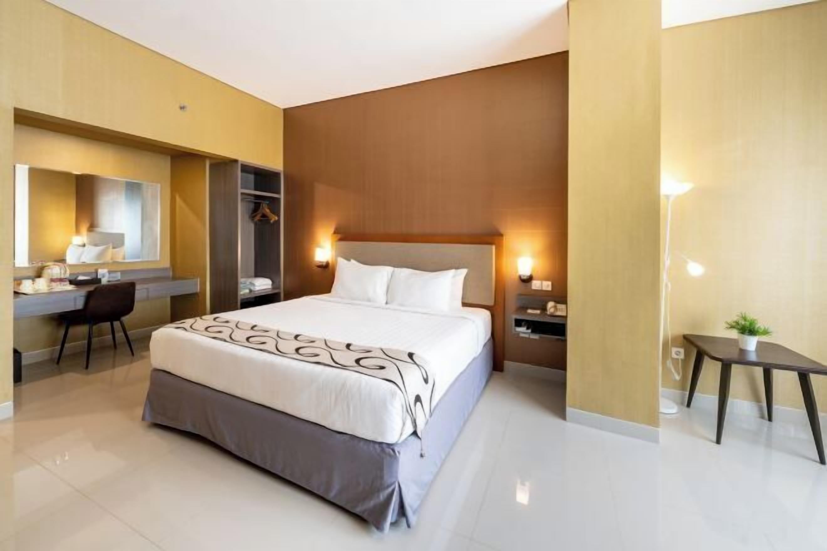 A hotel room with a bed, bedside tables, a desk, a chair, and a small table with a plant.