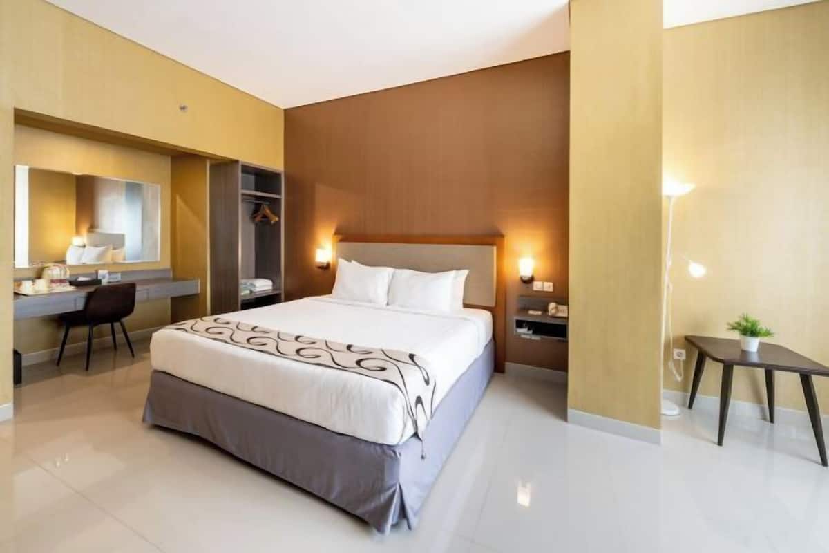 A hotel room with a bed, bedside tables, a desk, a chair, and a small table with a plant.