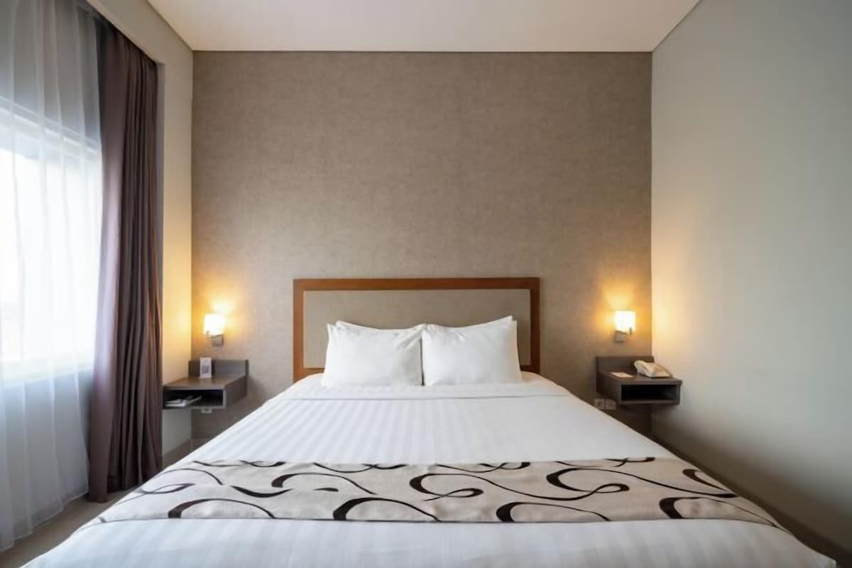 A hotel room with a large bed, two bedside tables with lamps, and a window with curtains.