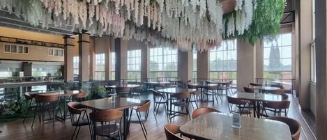 A restaurant with wooden tables and chairs, hanging floral decorations, and large windows.