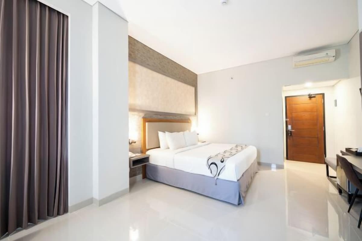 A modern hotel room with a large bed, bedside tables, a desk, and a wardrobe.