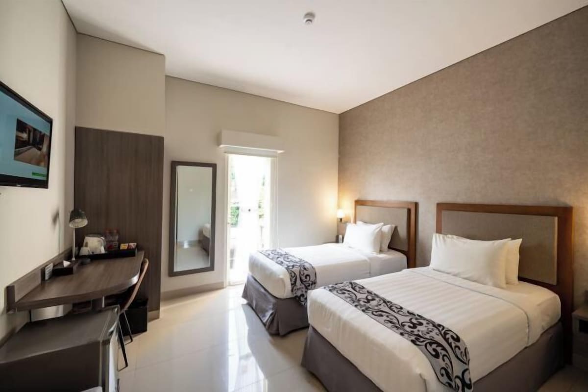 A hotel room with two beds, a desk, a mirror, and a window.