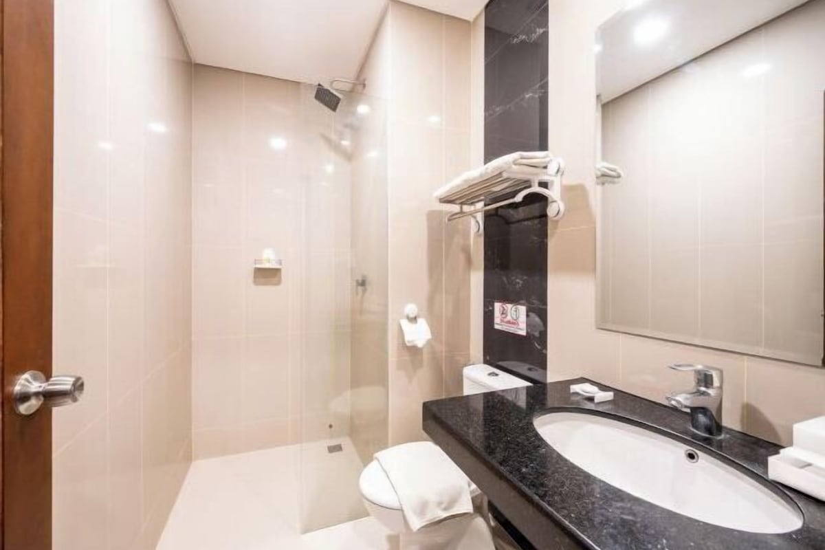 A modern bathroom with a glass-enclosed shower, a black marble sink, and a large mirror.