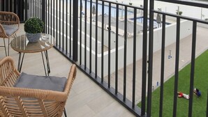 En balkon med fletstole, et glasbord og en potteplante.