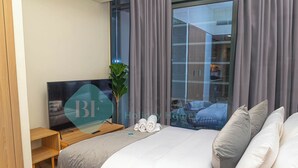 A modern hotel room with a large bed, a television, a small desk, and a window with curtains. - Bloomfields STU Balcony Azizi Riviera Meydan (Dubai)
