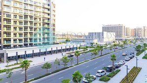 A modern building with multiple floors, large windows, and a parking area with cars and palm trees. - Bloomfields STU Balcony Azizi Riviera Meydan (Dubai)