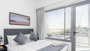Moderni hotellihuone, jossa on sänky, näköala kaupunkiin ja parveke, jossa on tuoleja.