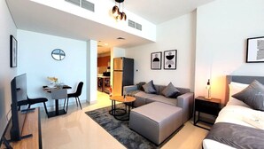 A modern, well-lit living room with a sofa, ottoman, and a dining area with a table and chairs. There is a kitchen visible in the background, and the room has a minimalist design with a large window and artwork on the walls. - Bloomfields STU with Canal View Julphar Al Reem (Abu Dabi)