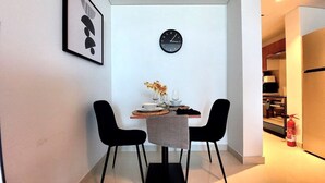 A modern dining area with a minimalist table, two black chairs, a clock on the wall, and a framed artwork. - Bloomfields STU with Canal View Julphar Al Reem (Abu Dabi)